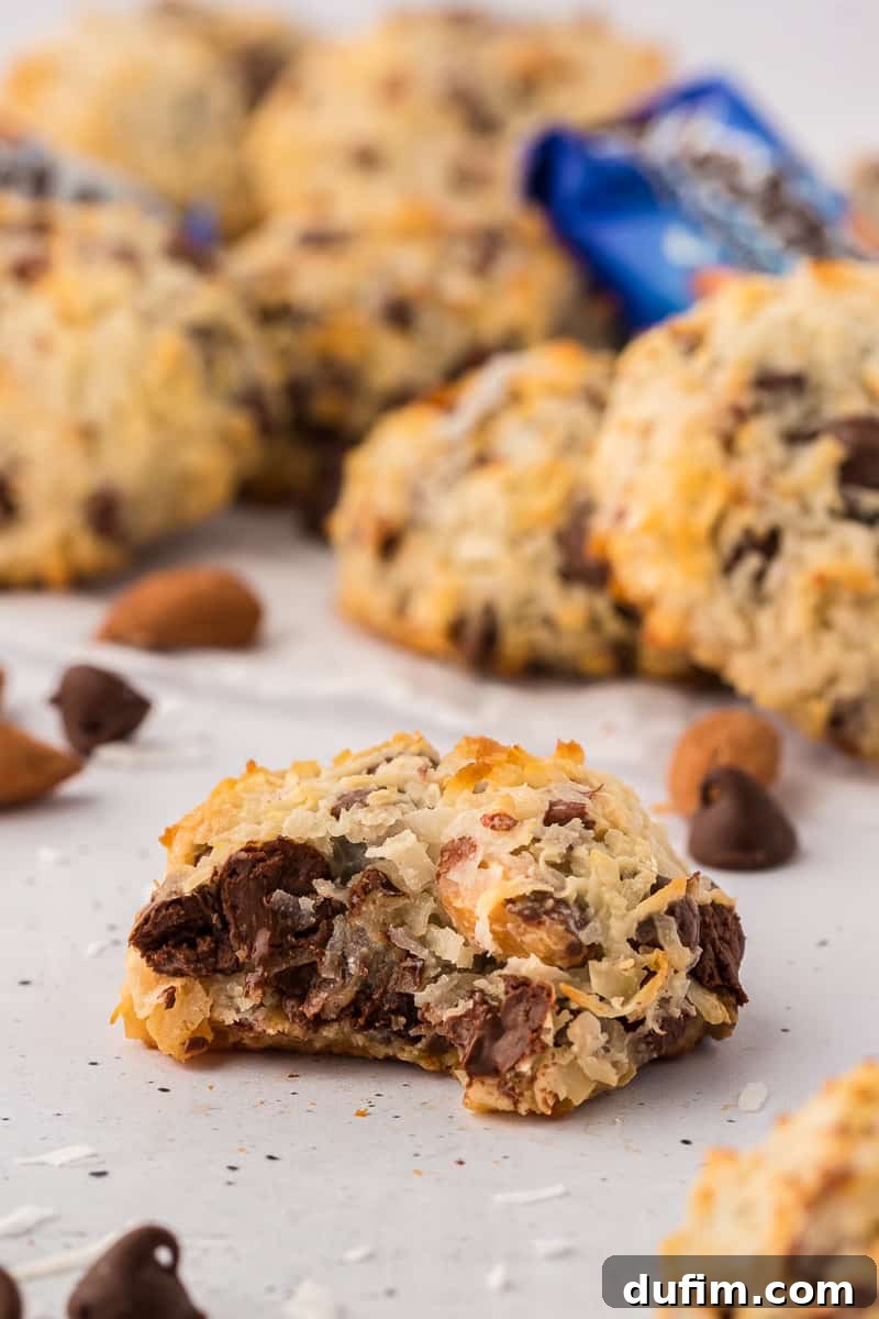 almond joy cookies arranged on a flat surface with chocolate chips and coconut flakes sprinkled around and a close up of one cookie with a bite of of it in the middle