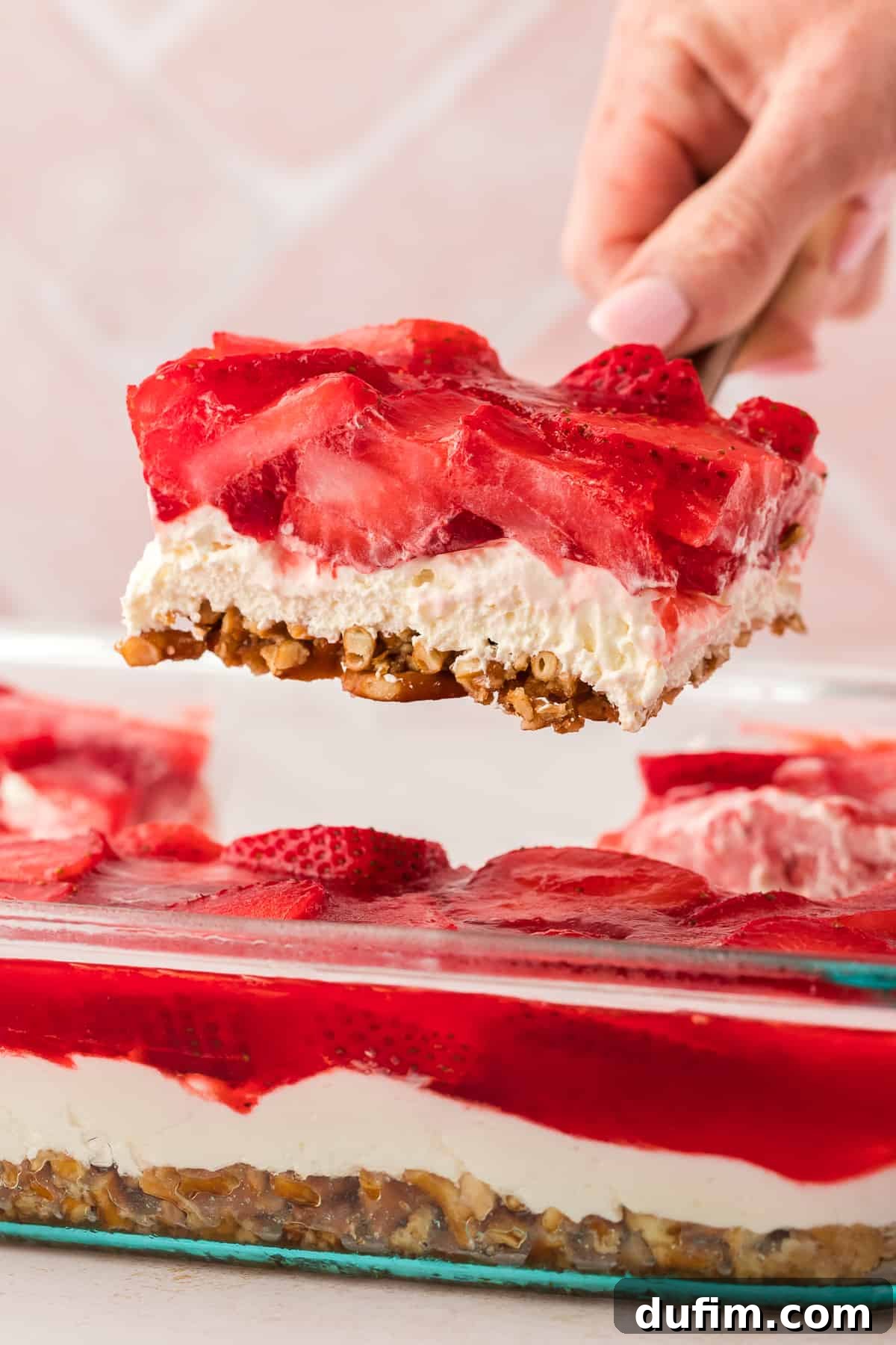 A slice of strawberry pretzel salad being lifted with a spatula out of a baking dish full of strawberry pretzel salad