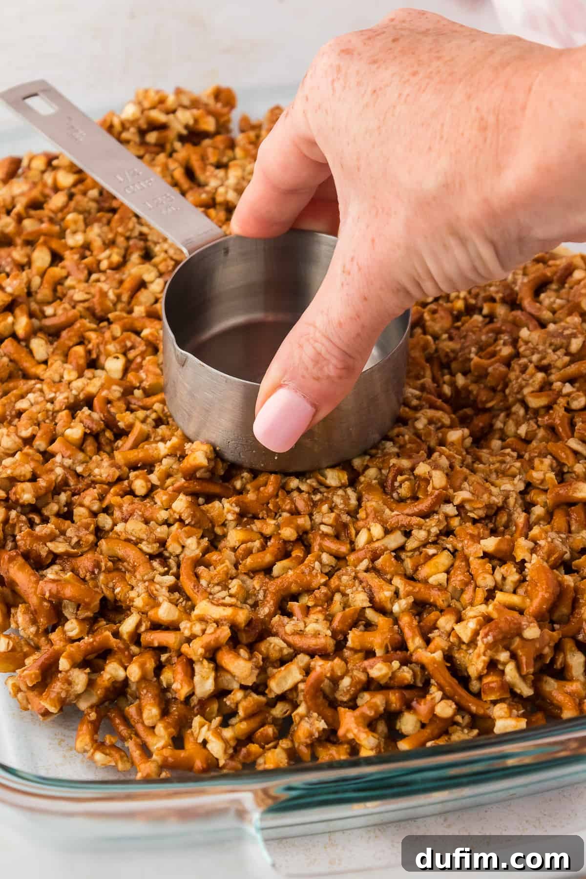 Using a measuring cup bottom to press down pretzel crust into the bottom of a baking dish