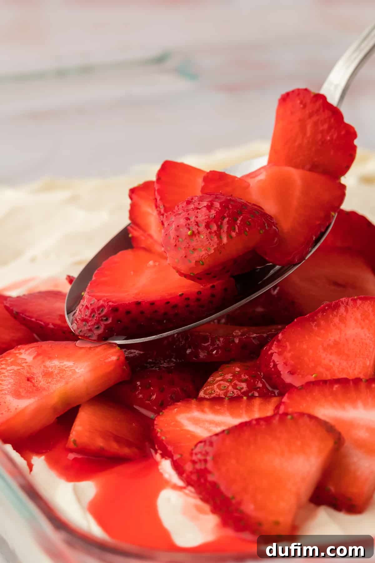 Strawberry mixture being spooned on top of the cream cheese layer of strawberry pretzel salad in a clear glass baking dish