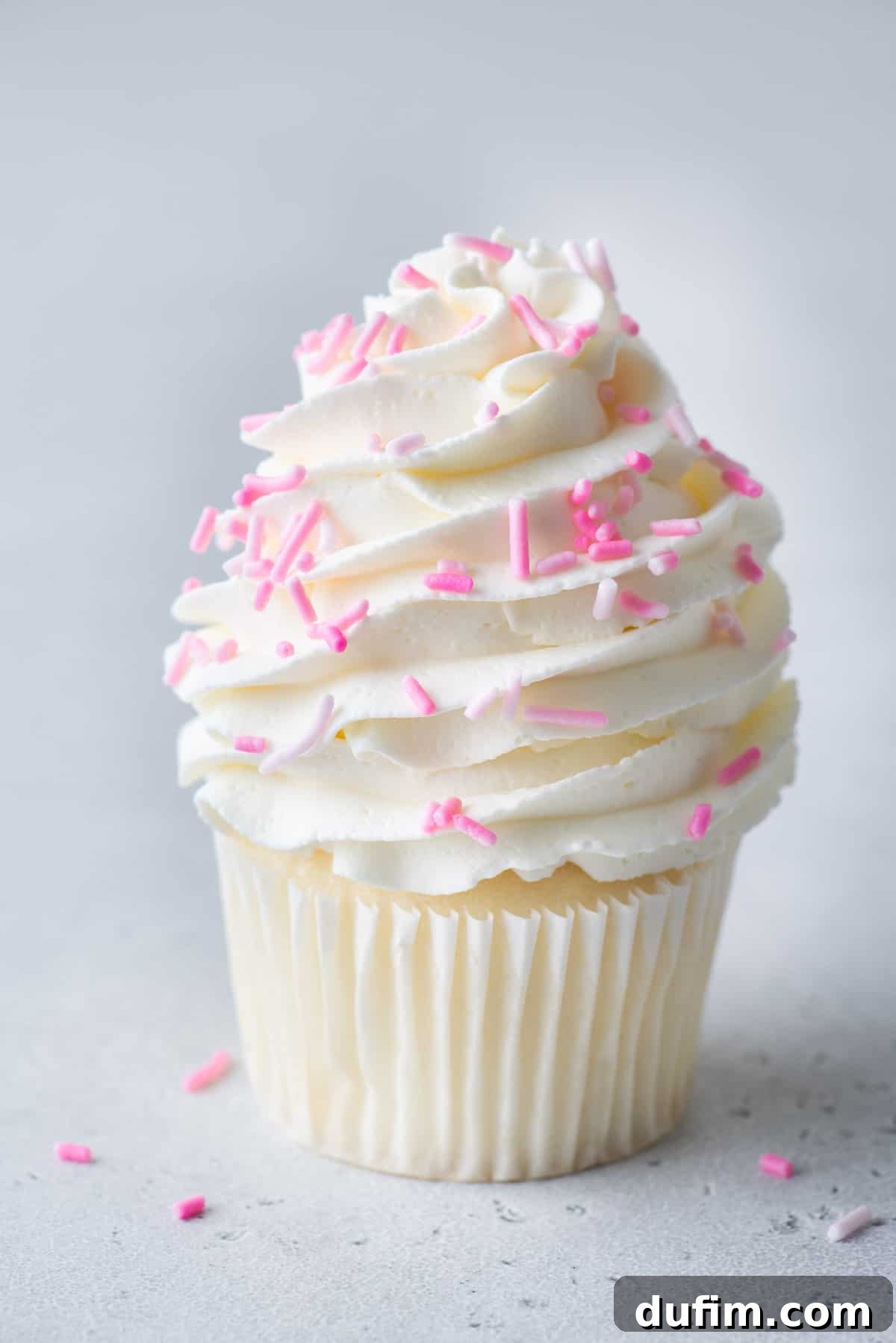 A vanilla cupcake topped with perfectly stabilized whipped cream and pink sprinkles, showcasing its firm and attractive shape.