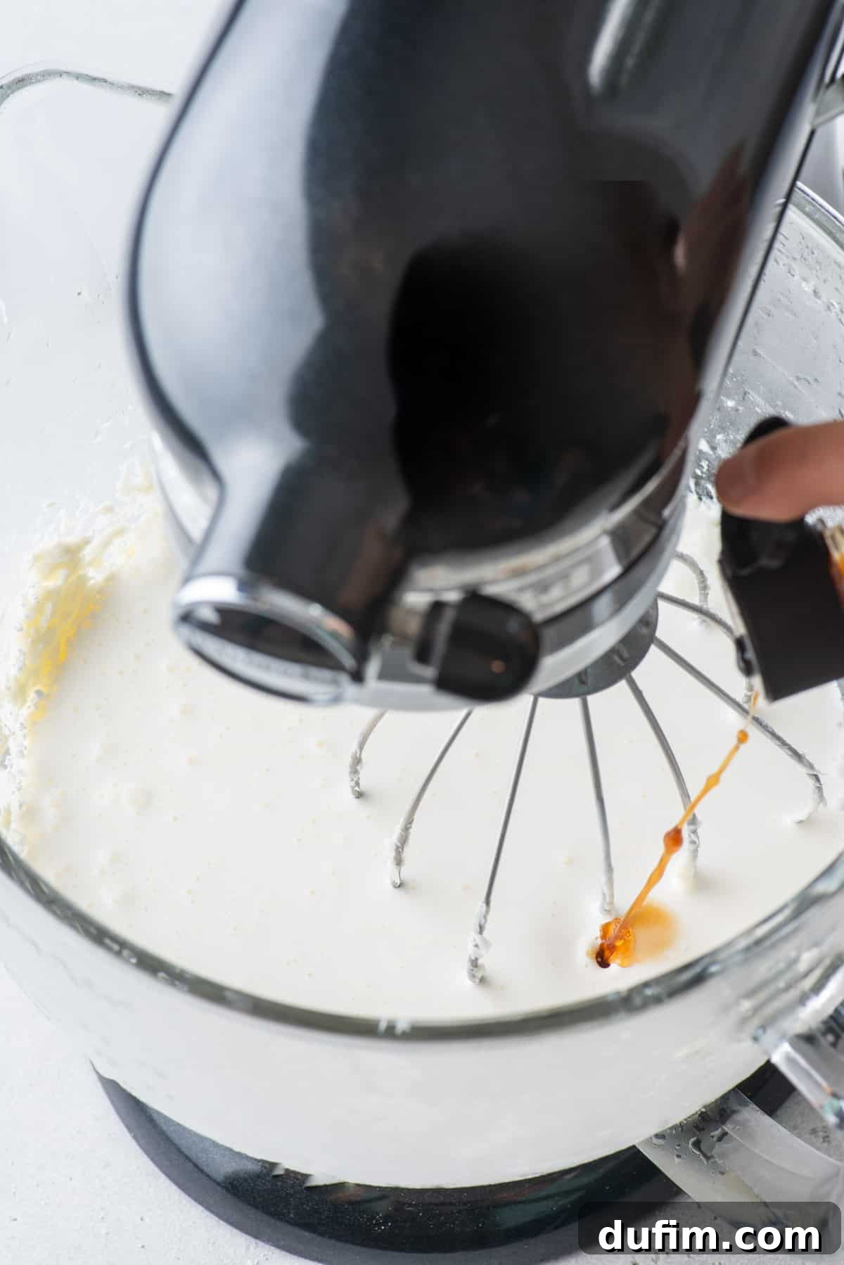 Vanilla extract being carefully added to the mixing bowl with the cream cheese and sugar mixture.