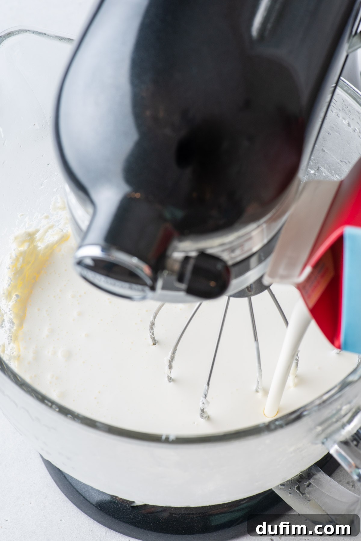 Cold heavy whipping cream being poured into the electric mixer, joining the other ingredients.