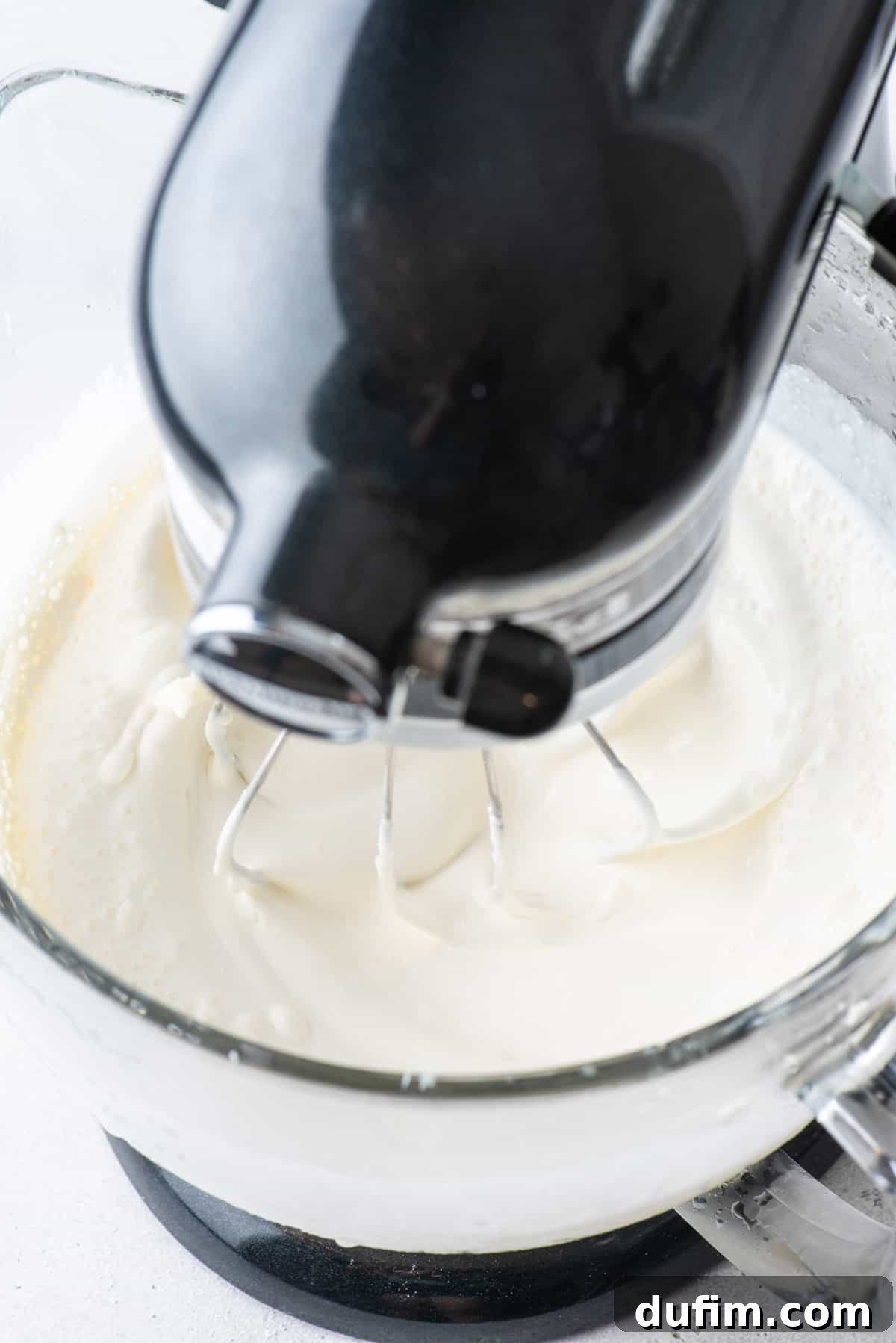 All ingredients for stabilized whipped cream being mixed thoroughly in an electric mixer, forming a cohesive, fluffy mixture.