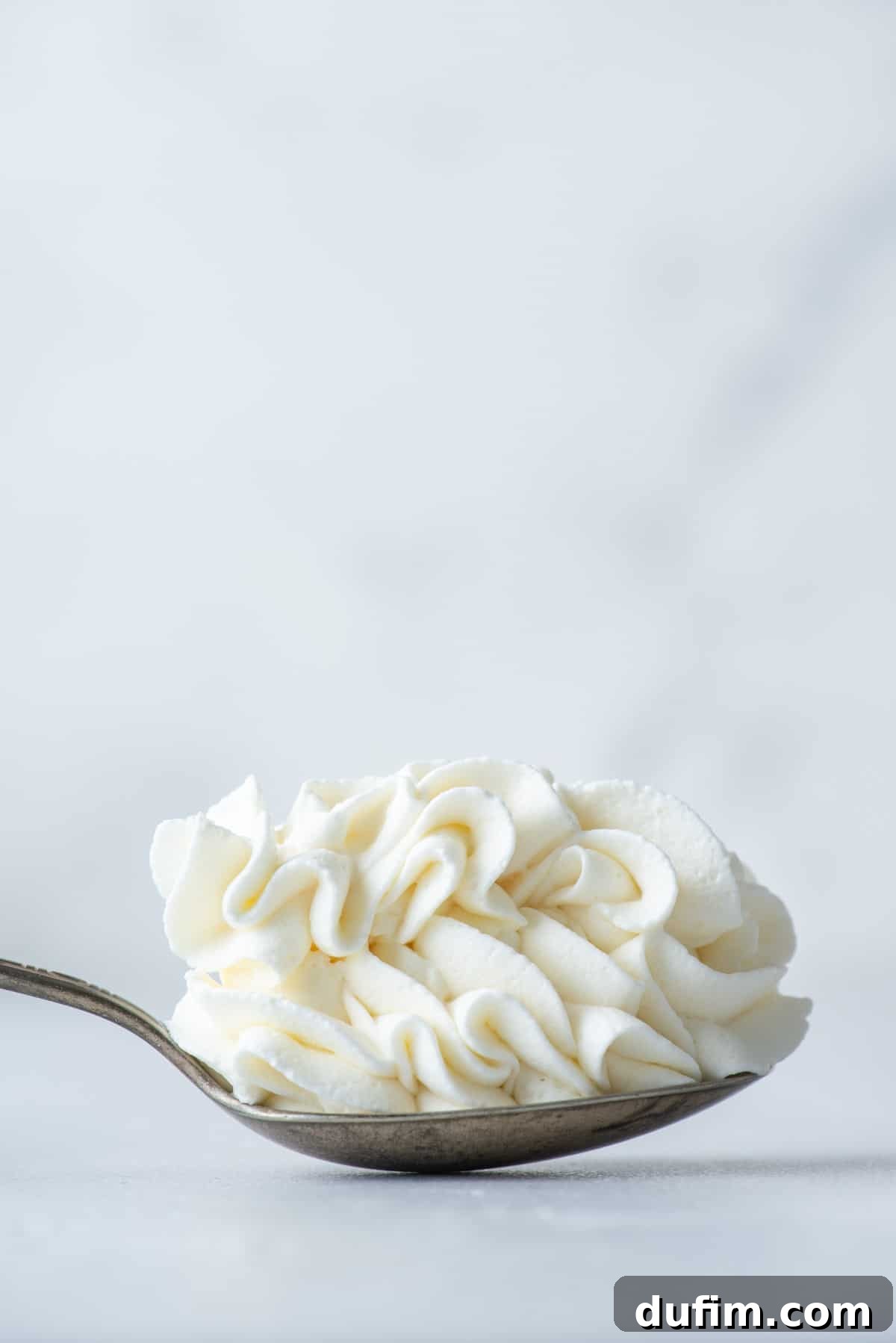 A spoon full of stabilized whipped cream resting on a flat surface, illustrating its firm and scoopable texture.