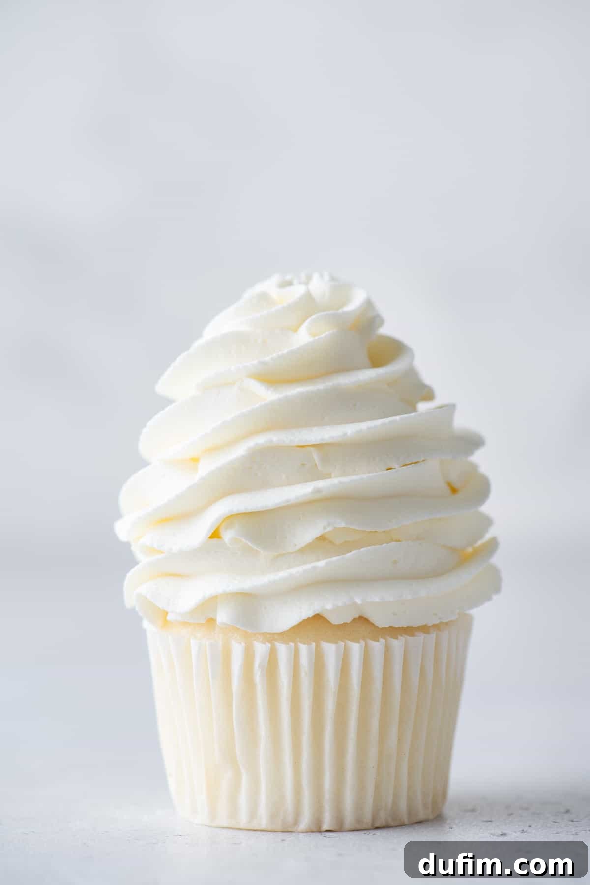 Stabilized whipped cream piped delicately on top of a vanilla cupcake, demonstrating its structured form.