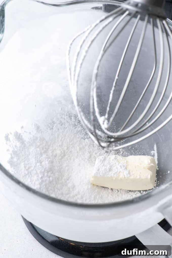 Softened cream cheese and powdered sugar being beaten together in an electric mixer until smooth.
