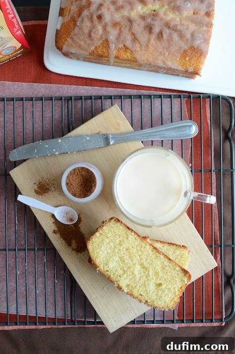 A freshly baked Whipped Eggnog Loaf Cake cooling on a rack, with a carton of eggnog nearby.