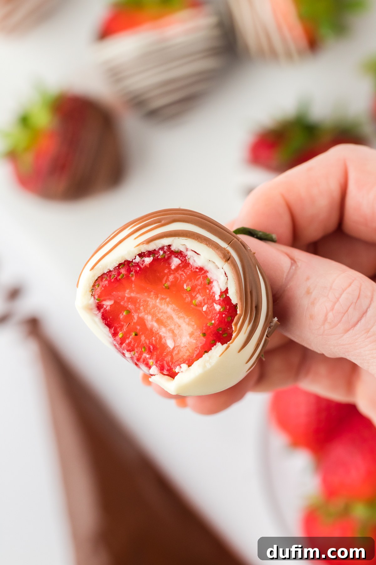 Irresistible Chocolate Dipped Strawberries 5 Close up of a hand holding a chocolate covered strawberry with a single bite taken out, revealing the fresh, vibrant red strawberry inside against the dark chocolate coating.