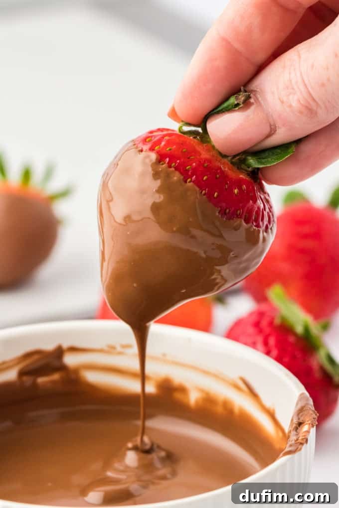 Irresistible Chocolate Dipped Strawberries 9 A strawberry perfectly dipped in melted chocolate, held above the bowl to allow excess chocolate to drip off, ensuring a smooth finish.