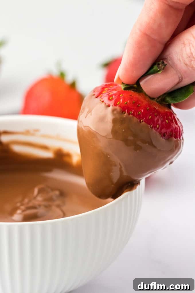 Irresistible Chocolate Dipped Strawberries 10 A close-up showing a chocolate-dipped strawberry being gently scraped along the inner edge of the chocolate bowl to remove excess coating, demonstrating the technique for a clean edge.