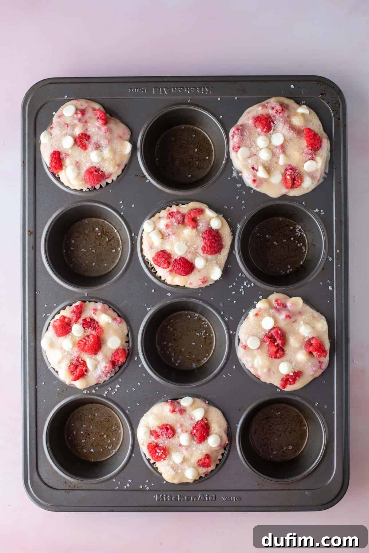 Decadent Raspberry White Chocolate Muffins 6 A 12-cup muffin pan, meticulously prepared with rich raspberry white chocolate chip muffin batter filling every other muffin hole, showcasing the strategic placement for achieving bakery-style tops.