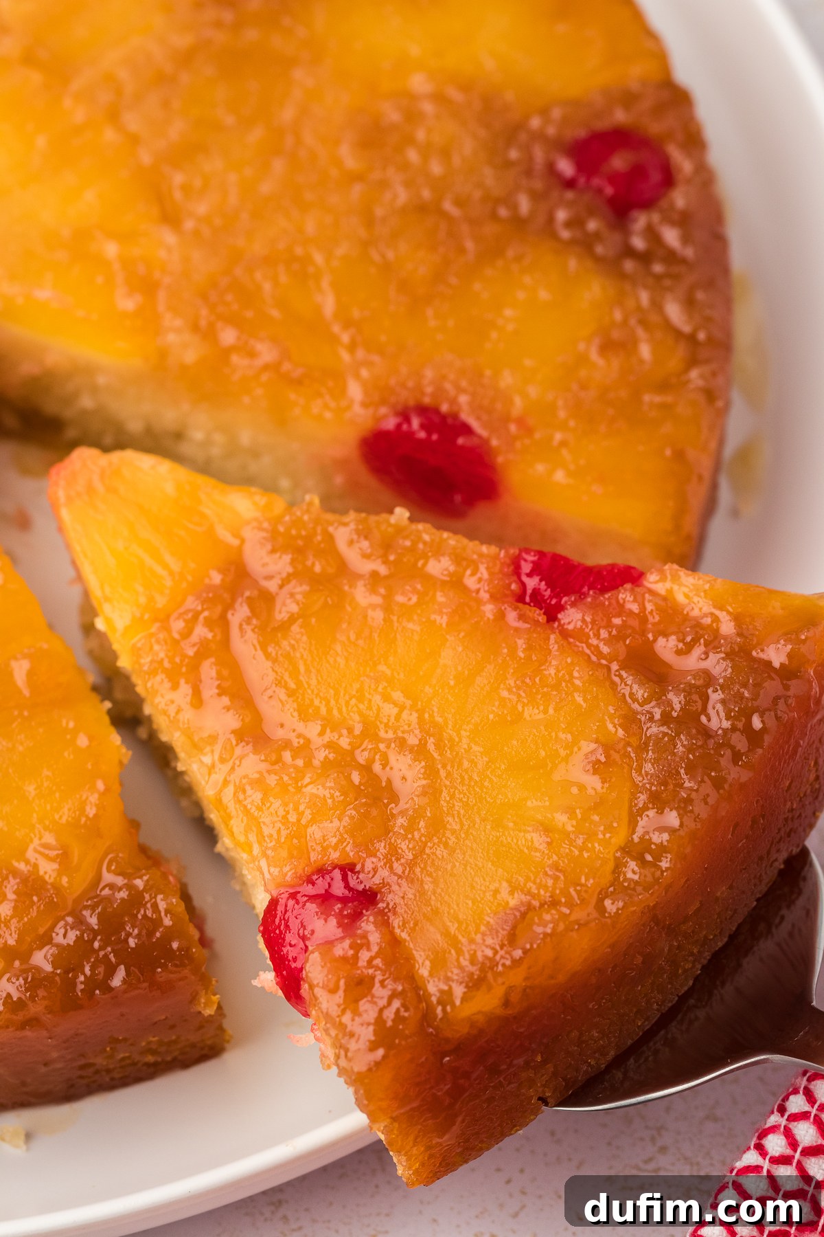 A close-up shot of a perfect slice of pineapple upside-down cake being delicately lifted away from the main cake, showcasing its moist texture and golden topping.