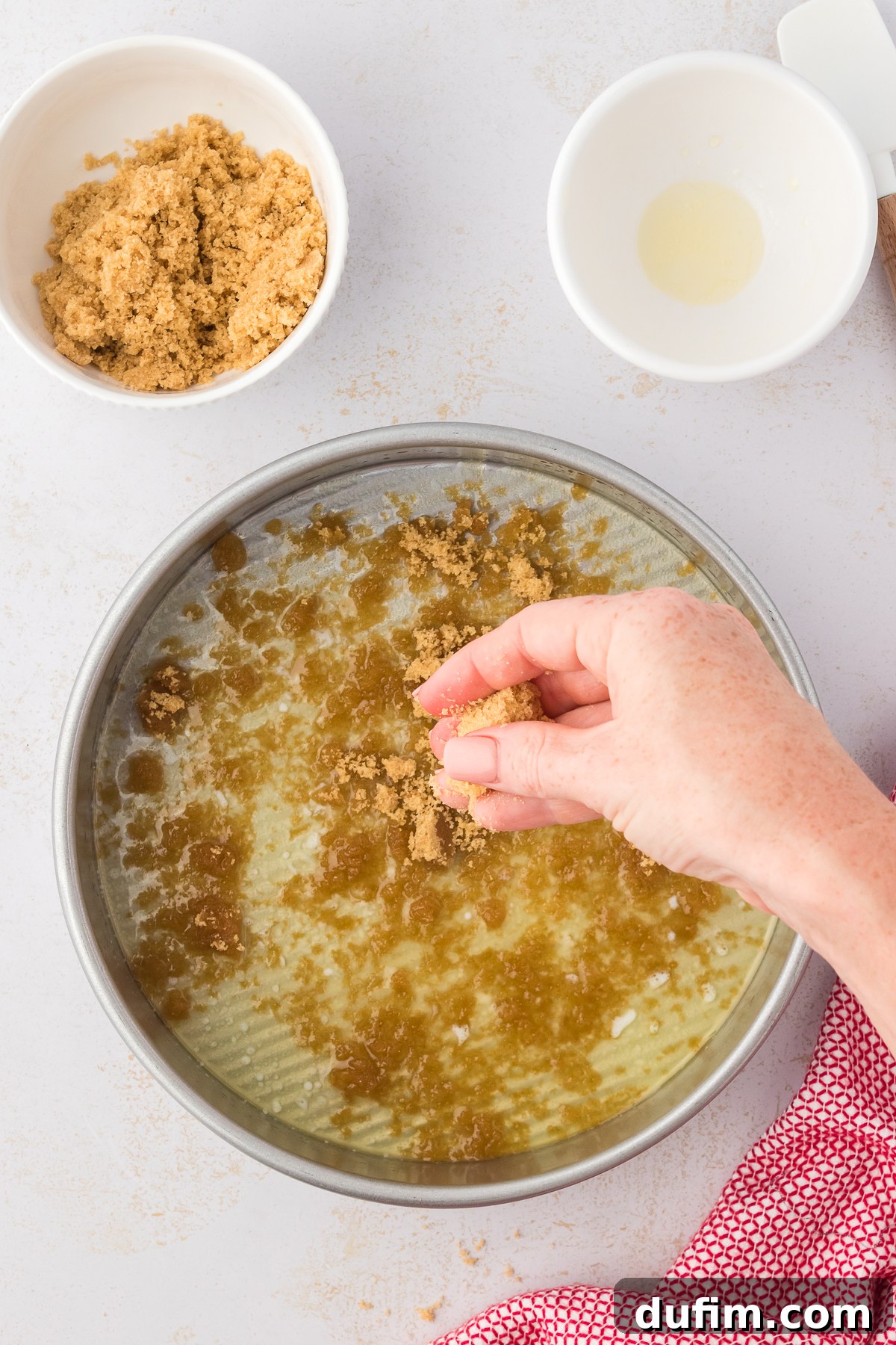 A round cake pan being prepared with a sprinkle of brown sugar over a layer of melted butter, essential for the cake's caramelized topping.