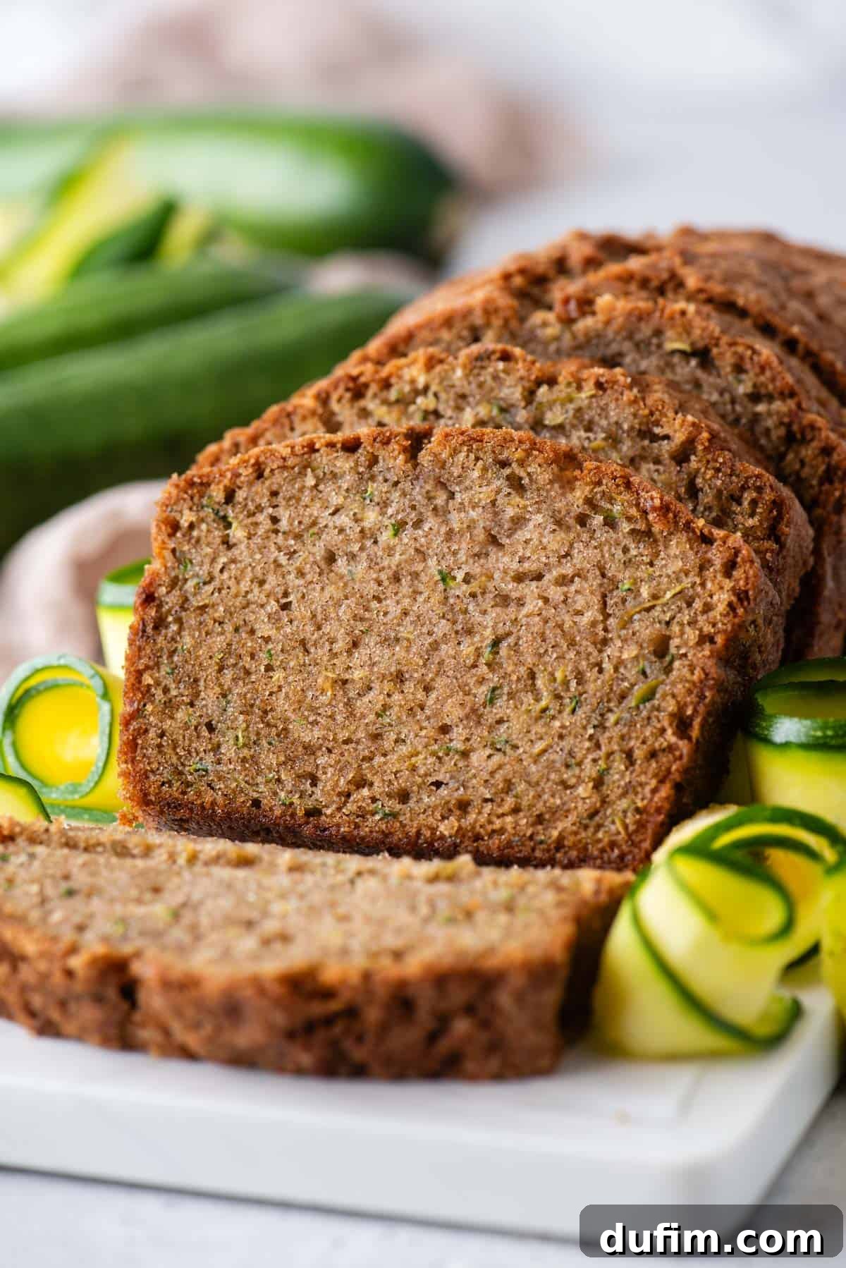 Irresistibly Moist Zucchini Bread 12 A vibrant close-up of a sliced loaf of zucchini bread, featuring its inviting texture, surrounded by fresh zucchini slices and whole zucchinis, capturing its homemade charm.