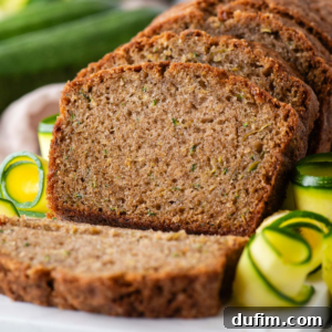 Beautifully sliced zucchini bread on a white plate with fresh zucchini peels artfully arranged around it, inviting a taste.