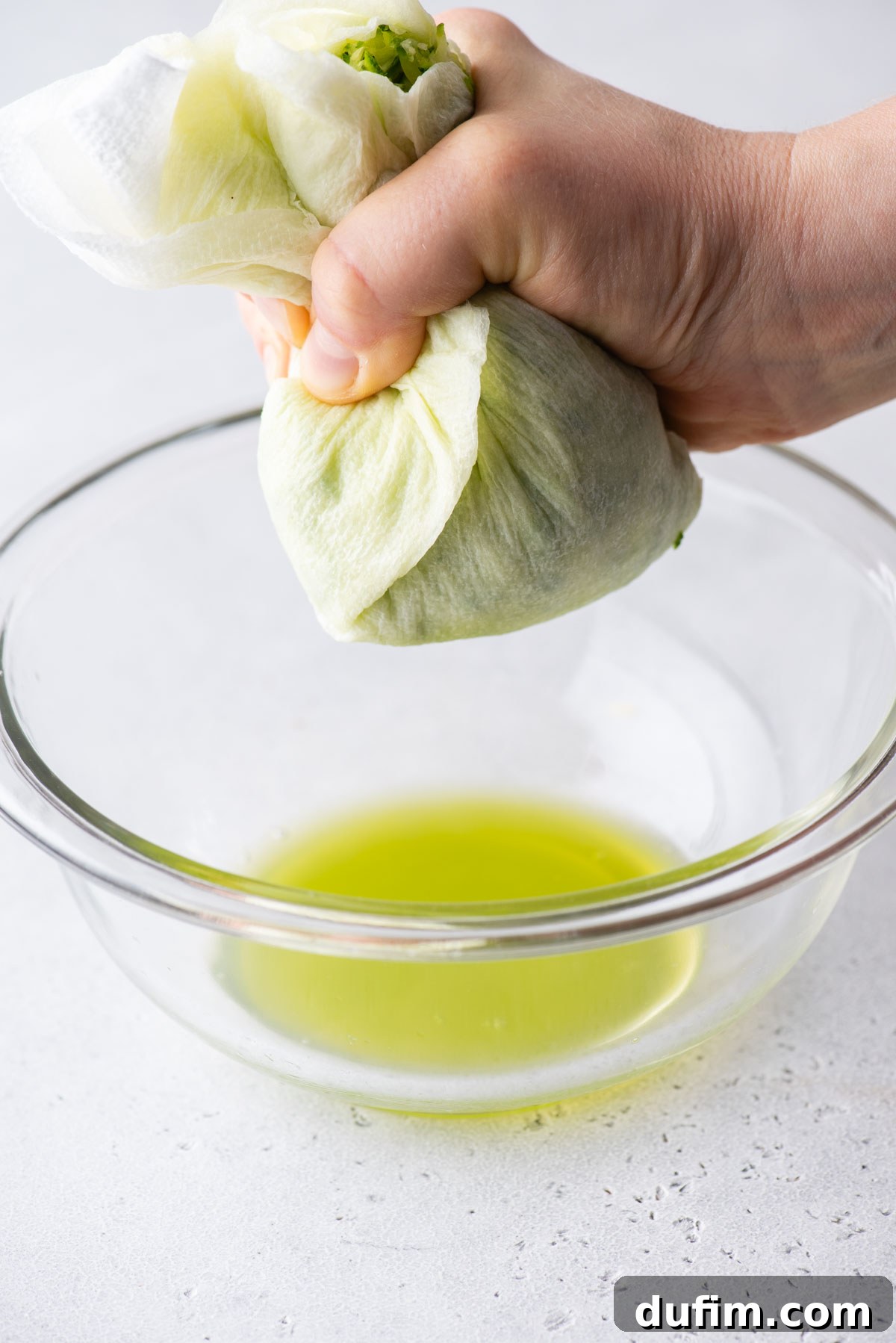 Irresistibly Moist Zucchini Bread 6 Hands squeezing excess moisture from shredded zucchini wrapped in paper towels over a clear glass bowl, a vital step for moist zucchini bread.