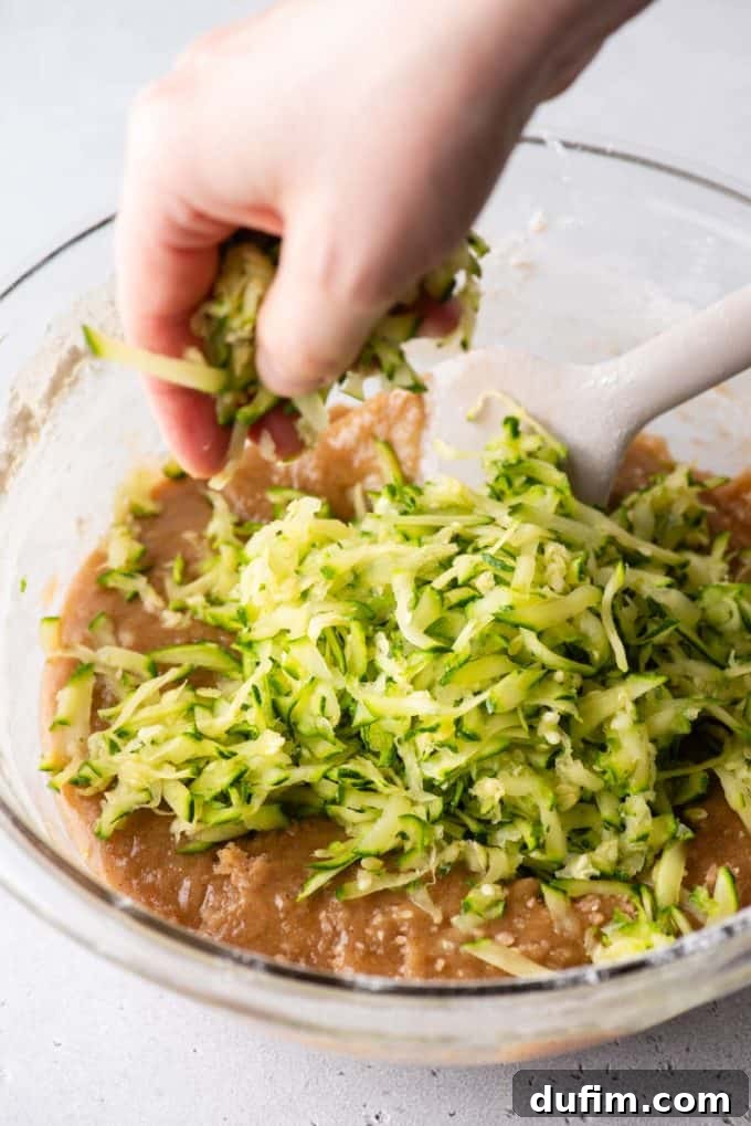Irresistibly Moist Zucchini Bread 7 Freshly shredded zucchini being gently added to a bowl of creamy bread batter, showing the key ingredient being incorporated.