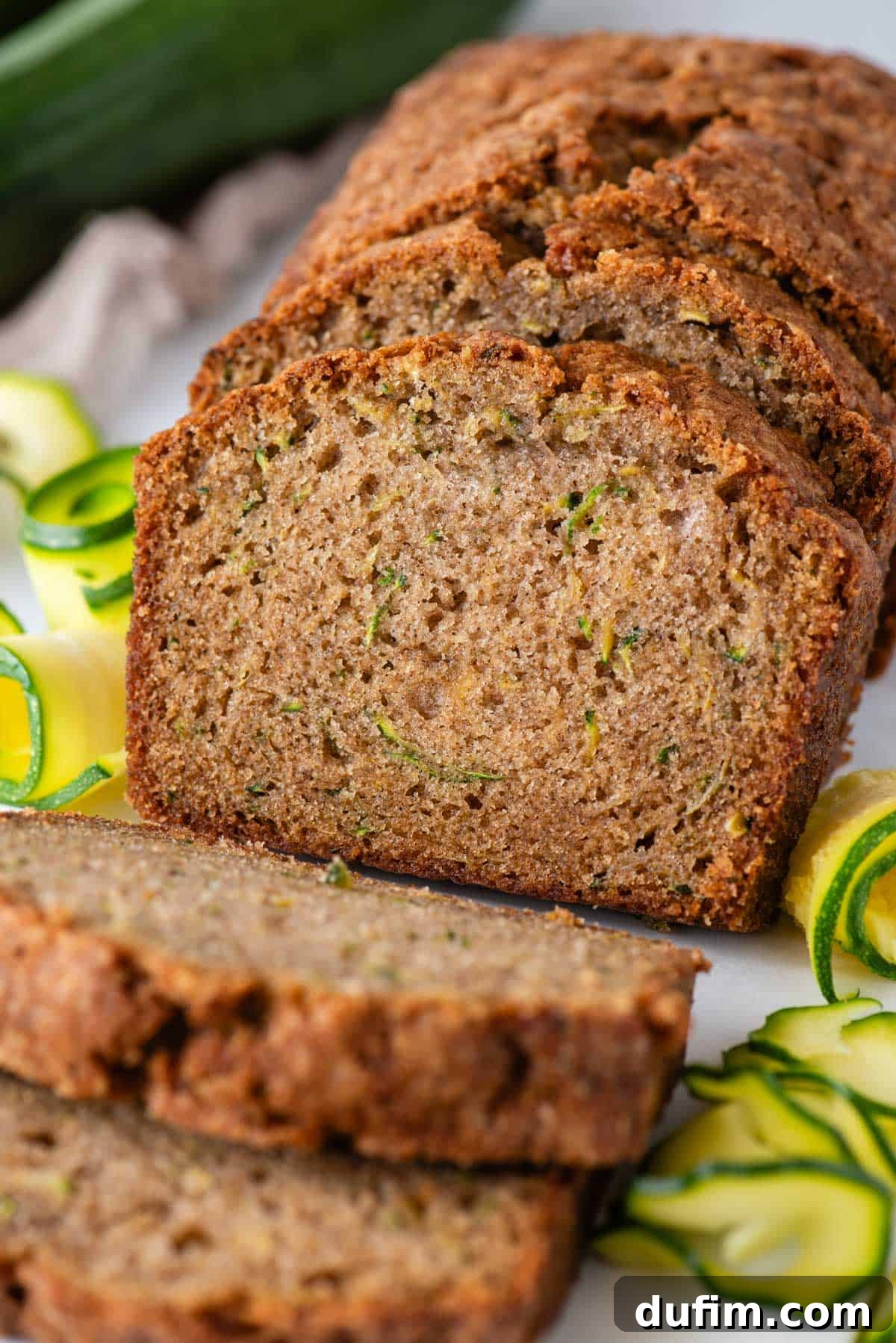 Irresistibly Moist Zucchini Bread 10 A close-up view of a perfectly sliced loaf of moist zucchini bread, showcasing its tender crumb, beautifully presented with fresh zucchini slices and whole zucchinis in the background.