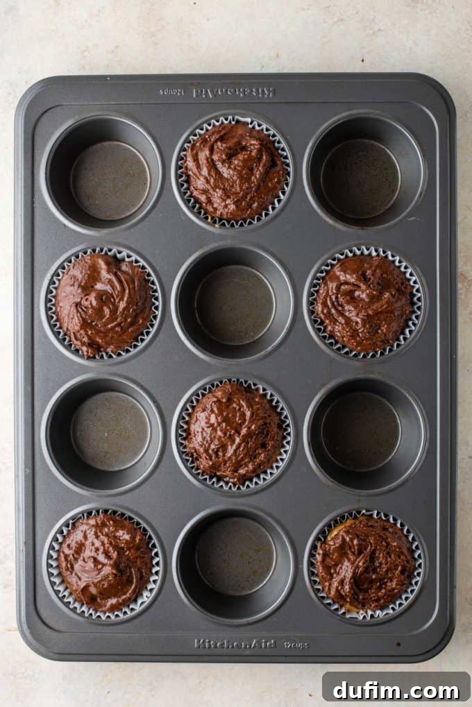 Muffin liners generously filled to the brim with chocolate peanut butter batter, showcasing ample portions ready for baking.