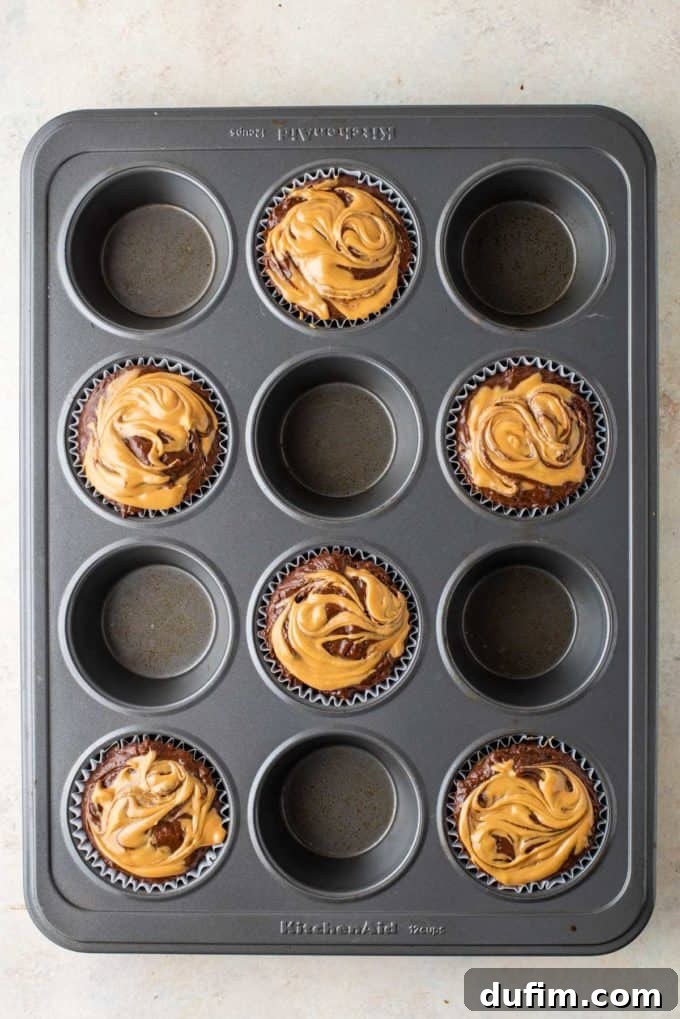 Muffin batter in a pan with artistically finished peanut butter swirls, waiting to be transformed by baking.