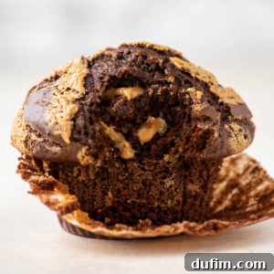 A perfectly baked chocolate peanut butter muffin, showcasing its height and delicious swirl, with the liner partially peeled to reveal its moist interior.