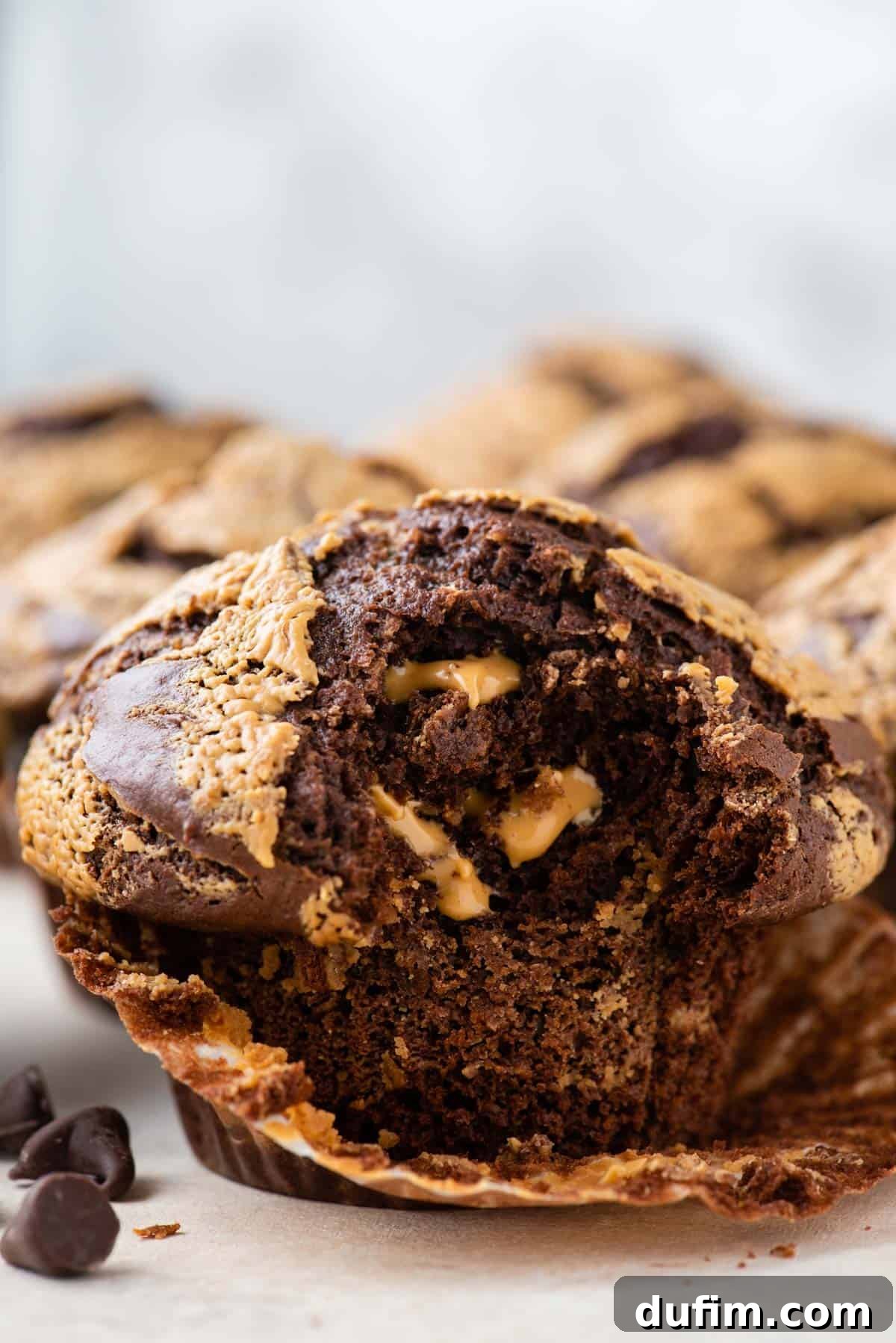 A close-up shot of a chocolate peanut butter muffin with its paper liner partially peeled down and a delicious bite taken out, revealing its moist and rich interior.