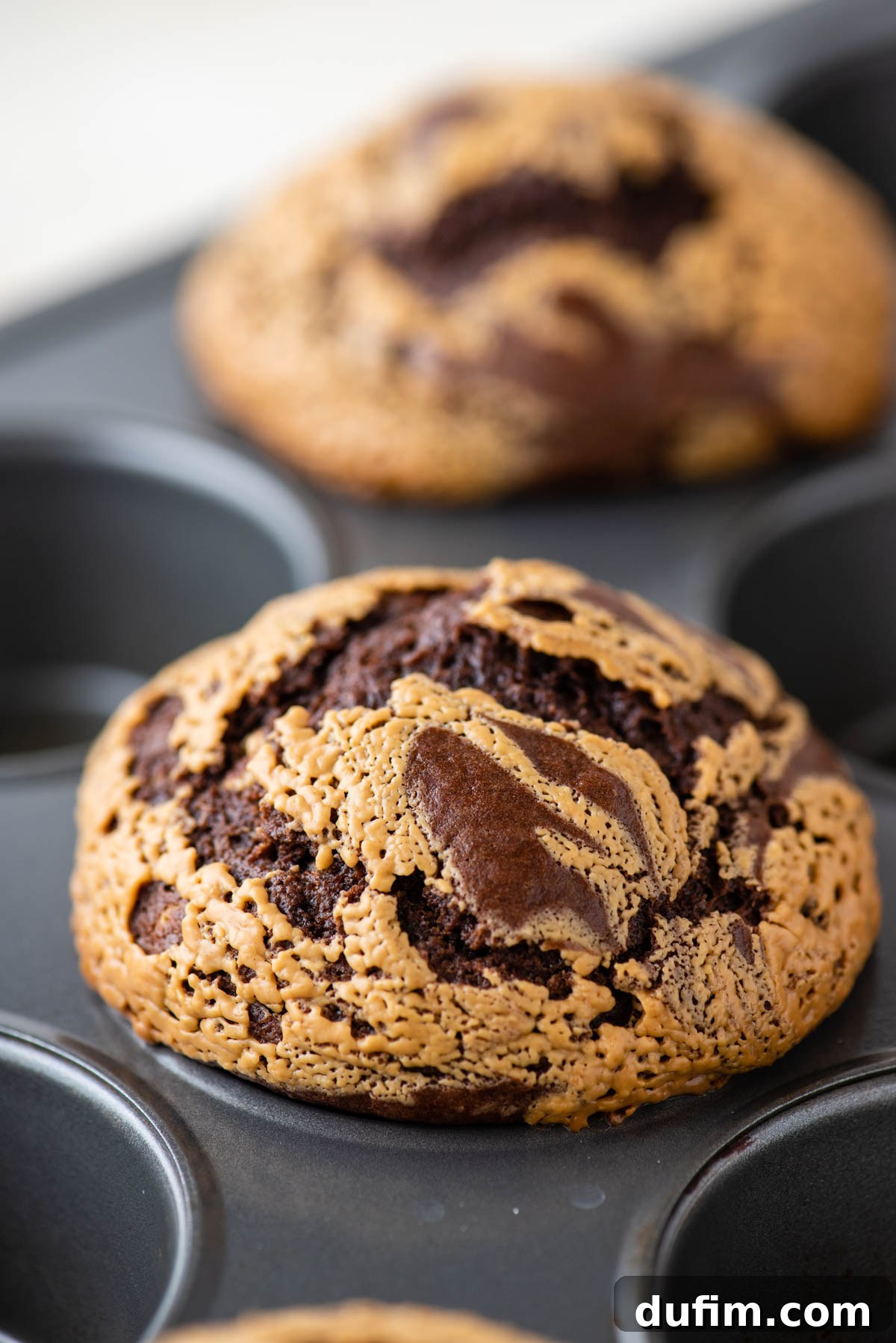 A close-up view of a muffin tin filled with unbaked chocolate peanut butter muffin batter, clearly showing the distinctive swirled peanut butter on top.
