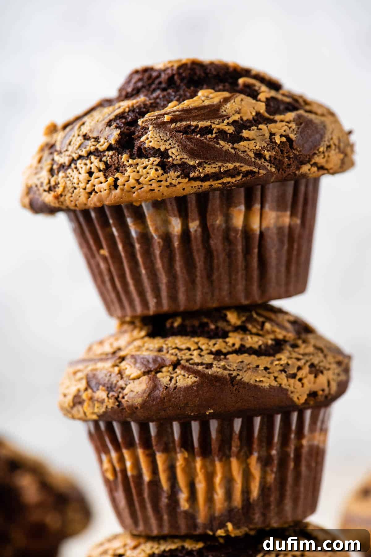 Two rich chocolate peanut butter muffins stacked on top of each other, highlighting their height and generous filling.