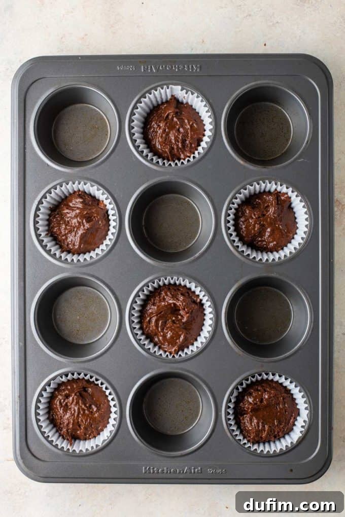 Chocolate muffin batter carefully scooped into every other paper liner in a 12-cup muffin pan, forming the initial base layer.