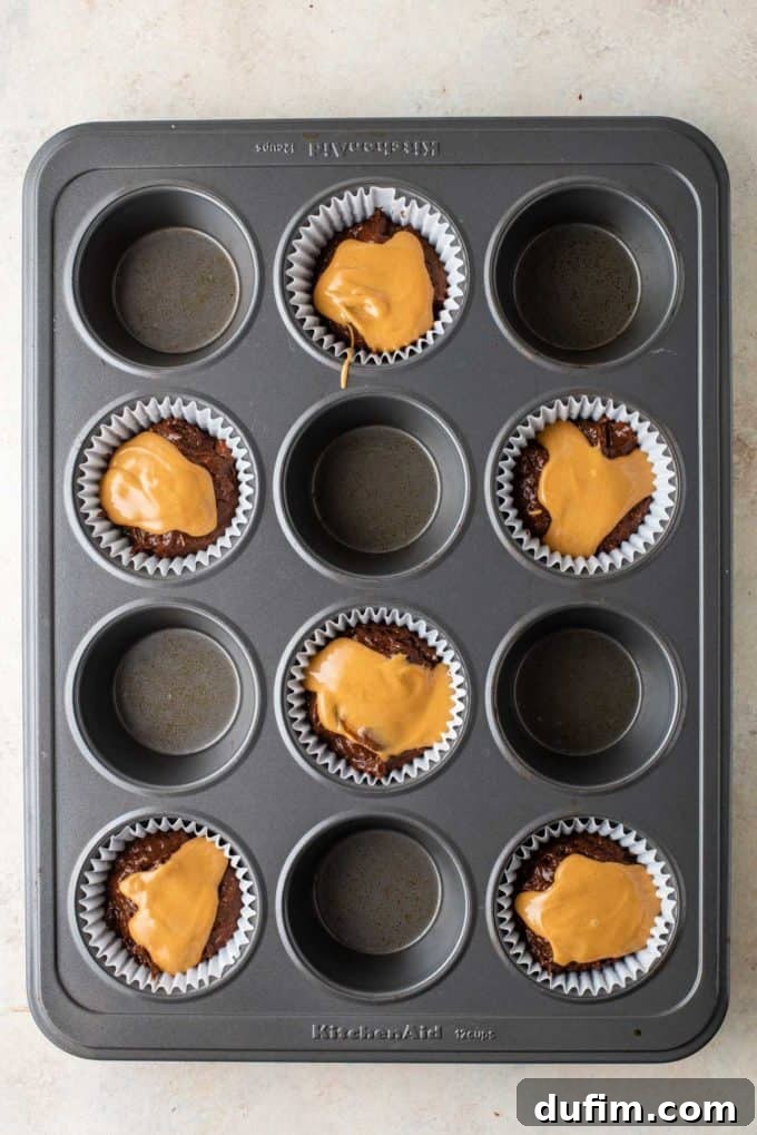 Muffin batter in a muffin pan with a generous dollop of melted peanut butter placed on top of the first chocolate layer, ready for swirling.