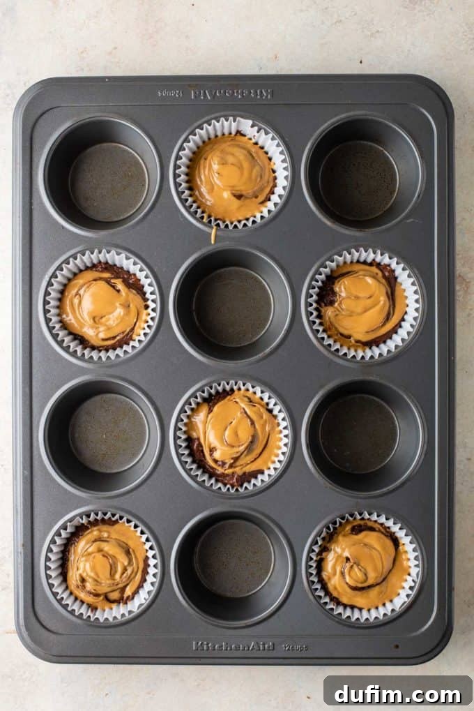Muffin batter in a pan with melted peanut butter swirled into the first layer, displaying an appealing marbled effect.