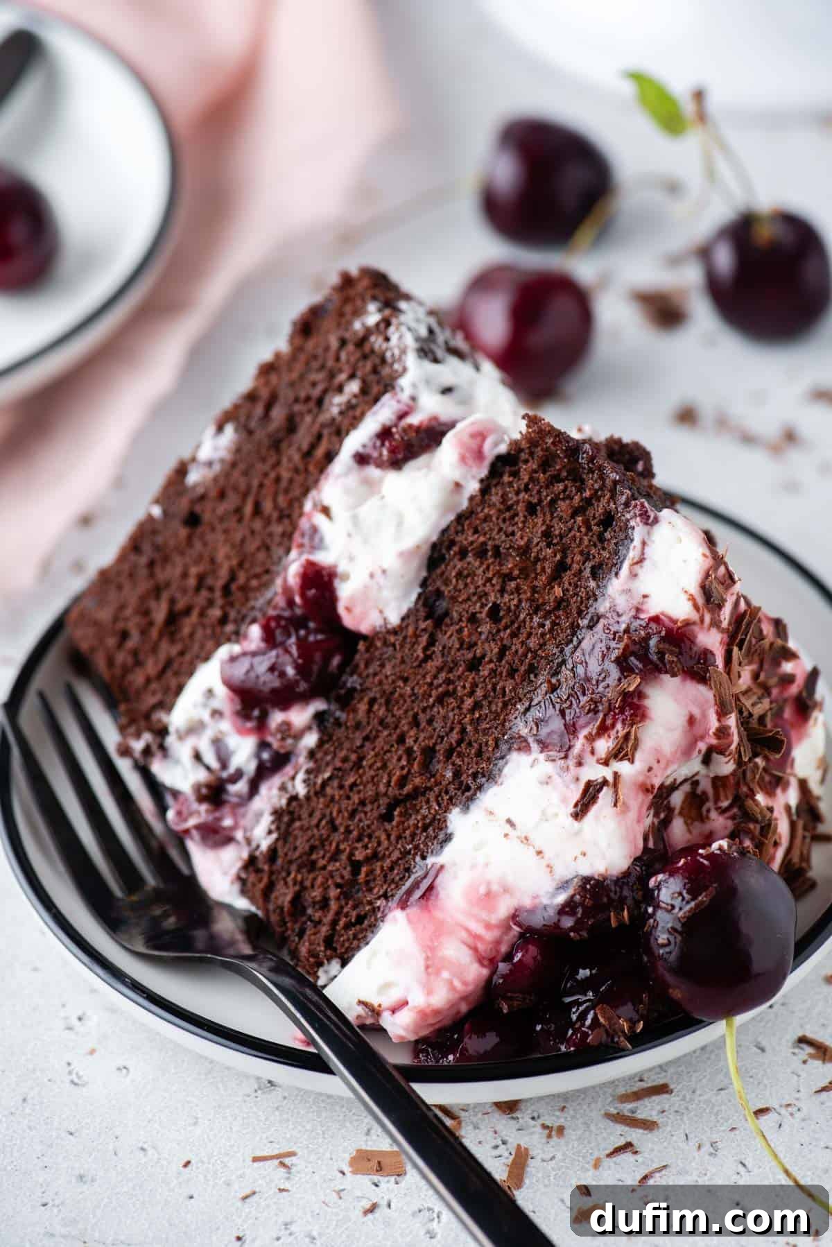 Decadent Black Forest Cherry Torte 5 a slice of black forest ake on a plate with a fork surrounded by cherries and little pieces of shaved chocolate
