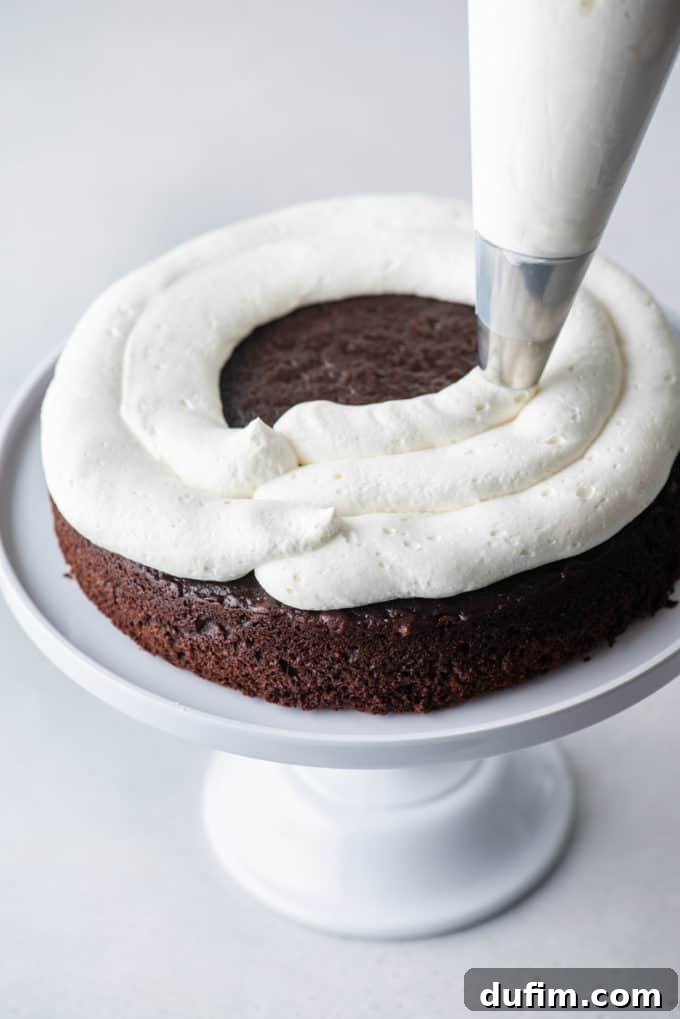 Decadent Black Forest Cherry Torte 7 one layer of chocolate cake on a white cake stand with stabilized whipped cream being piped on top