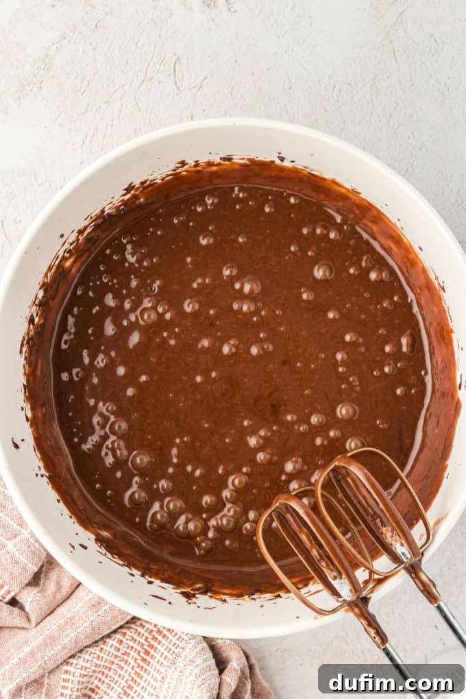Fully mixed Texas Sheet Cake batter in a white bowl, with clean electric mixer beaters leaning against the bowl, ready for baking.