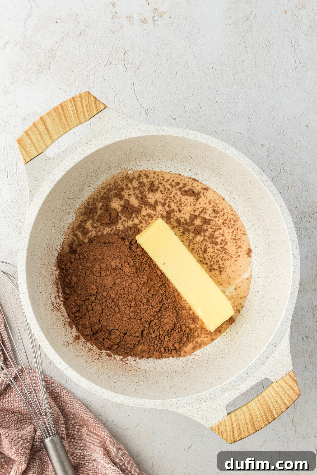 Milk, cocoa powder, and butter gathered in a saucepan, ready to be heated for the Texas Sheet Cake frosting, with a whisk nearby.