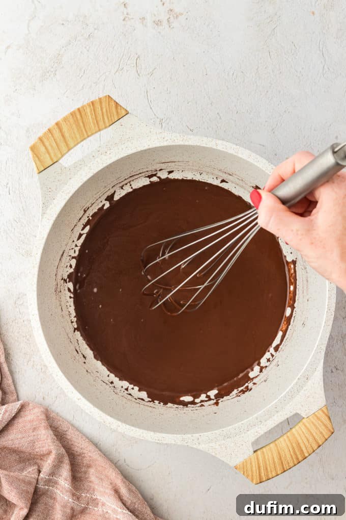 Chocolate frosting mixture being whisked in a saucepan over low heat, achieving a smooth and glossy texture.