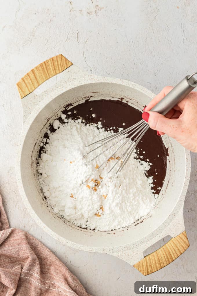 Powdered sugar being whisked into the warm chocolate mixture in a saucepan, creating the smooth Texas Sheet Cake frosting.
