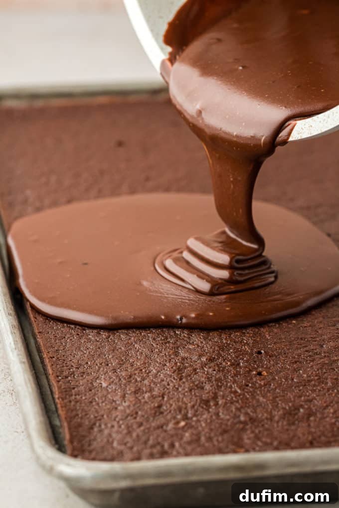 Warm chocolate frosting being generously poured over the freshly baked Texas Sheet Cake, creating a glossy, even layer.