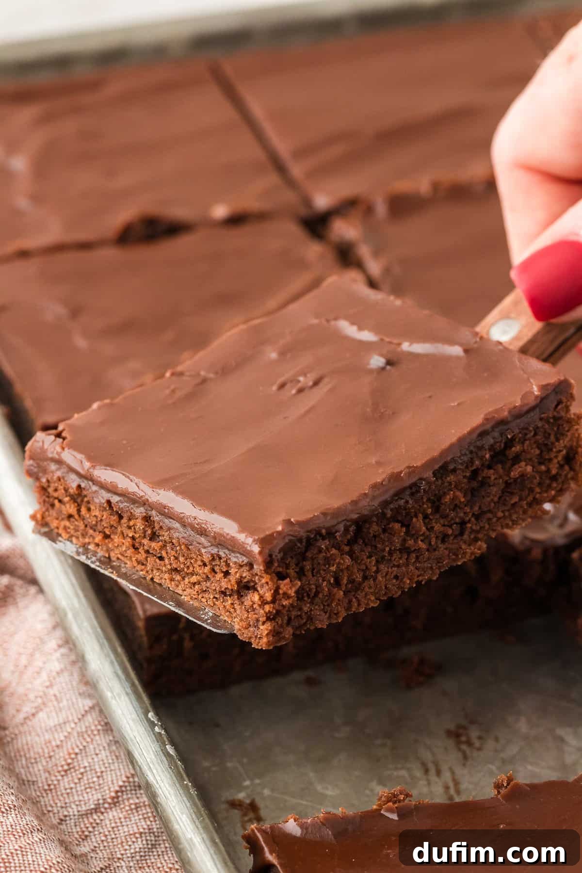 A slice of Texas Sheet Cake being carefully lifted out of a sheet pan filled with perfectly cut cake squares, ready to be served.