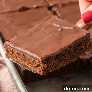 A slice of Texas Sheet Cake being lifted out of a sheet pan full of slices of cake, showcasing its perfection.