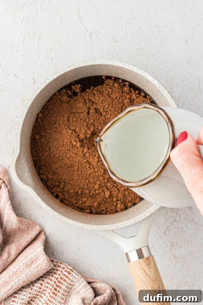 Water being poured into a saucepan with vegetable oil and cocoa powder, the starting wet ingredients for the Texas Sheet Cake.