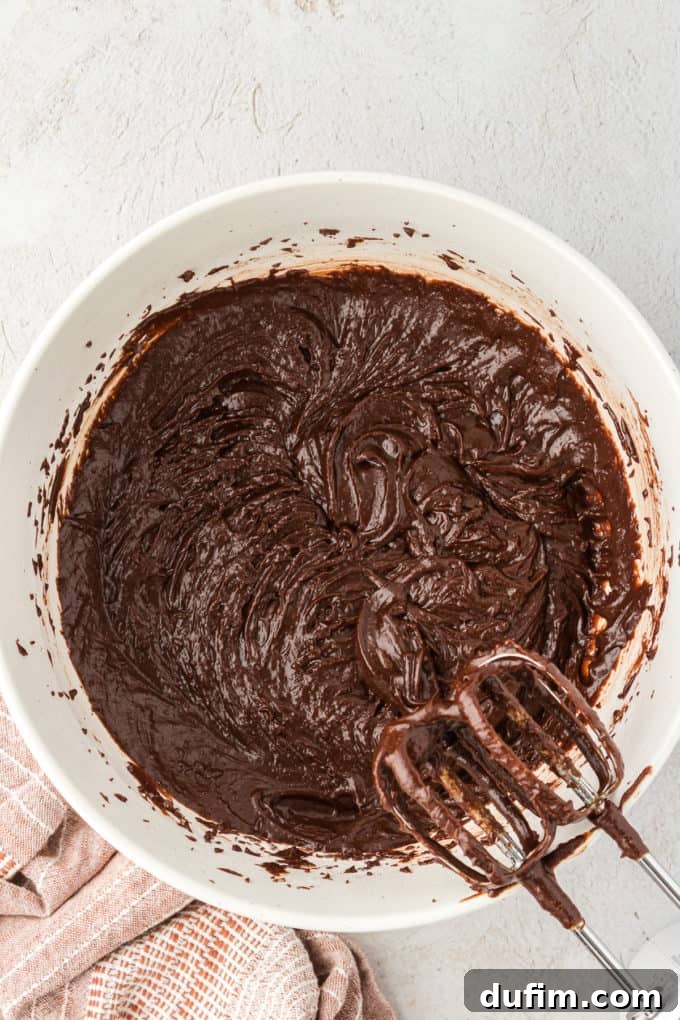 Texas Sheet Cake batter, partially mixed, in a white bowl with electric mixer beaters resting on the side, showing a smooth, consistent texture.