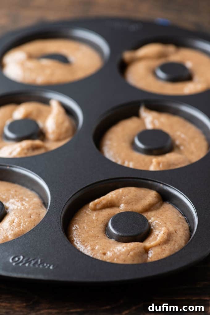 A donut pan filled with perfectly piped apple cider donut batter, uniform and smooth, ready to be transferred to the oven for baking.