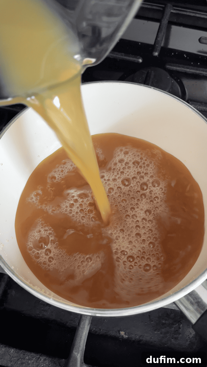 Carefully pouring fresh apple cider into a pristine white saucepan on the stovetop, initiating the first step for the flavor concentration.