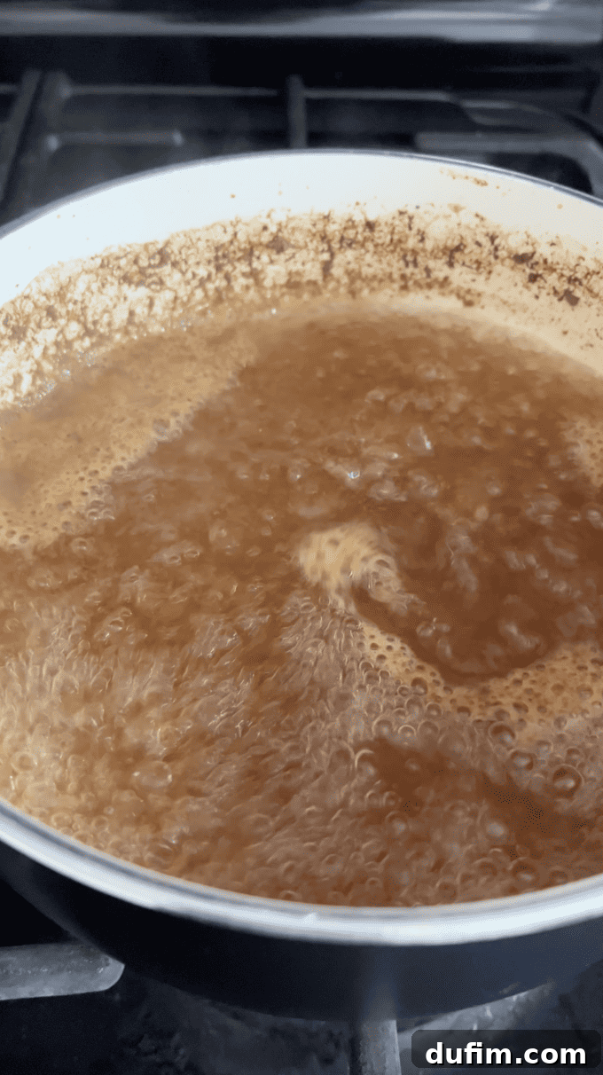 Apple cider actively boiling in a white saucepan over medium heat, visibly reducing and concentrating its natural flavors, a crucial step for intensely flavored donuts.