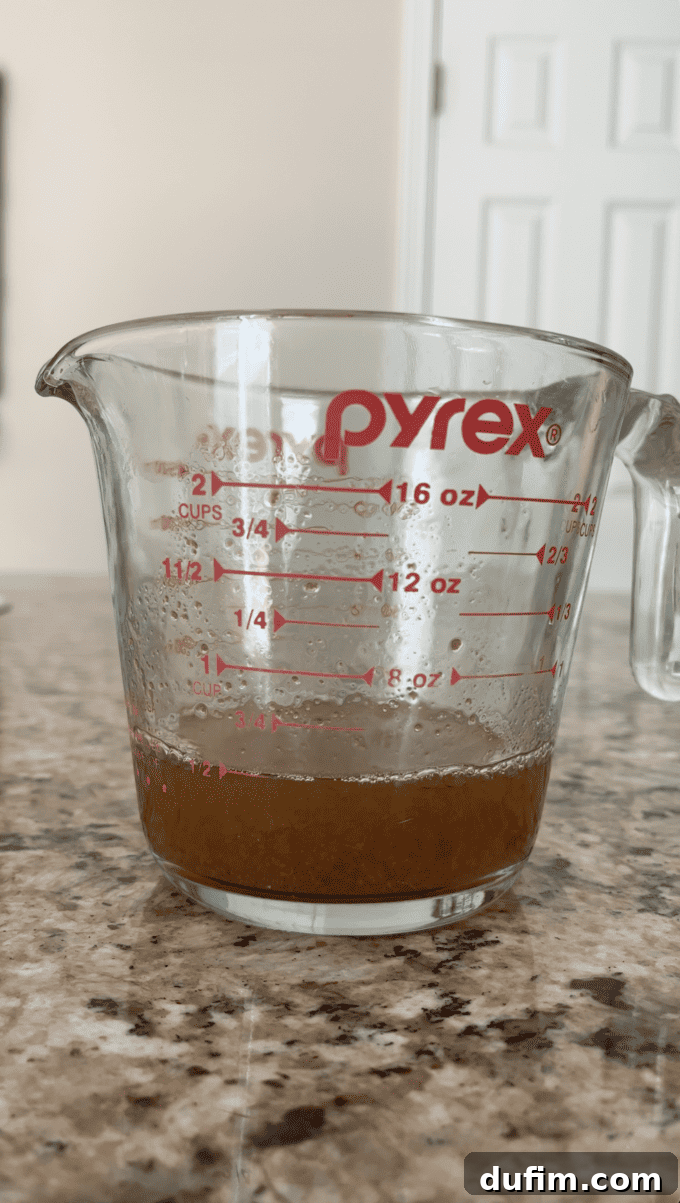 A measuring cup precisely holds 1/2 cup of deeply colored, aromatic reduced apple cider, showcasing the successful concentration of flavor essential for the delicious donuts.