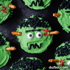 A finished Frankenstein cupcake with candy eyeballs, black sprinkles for hair, red stitches, and pretzel stick bolts.