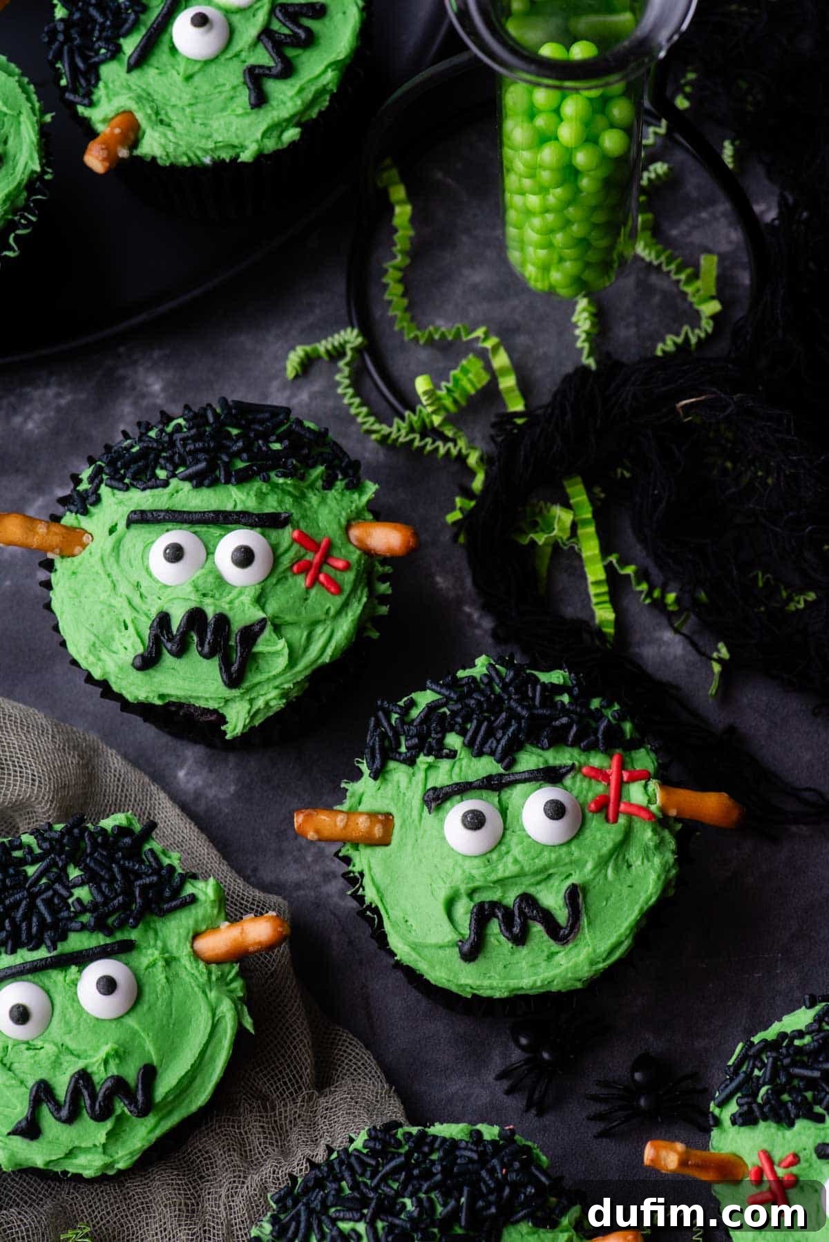Frankenstein cupcakes arranged on a grey surface, adorned with green sprinkles and tiny streamers, creating a festive Halloween atmosphere.