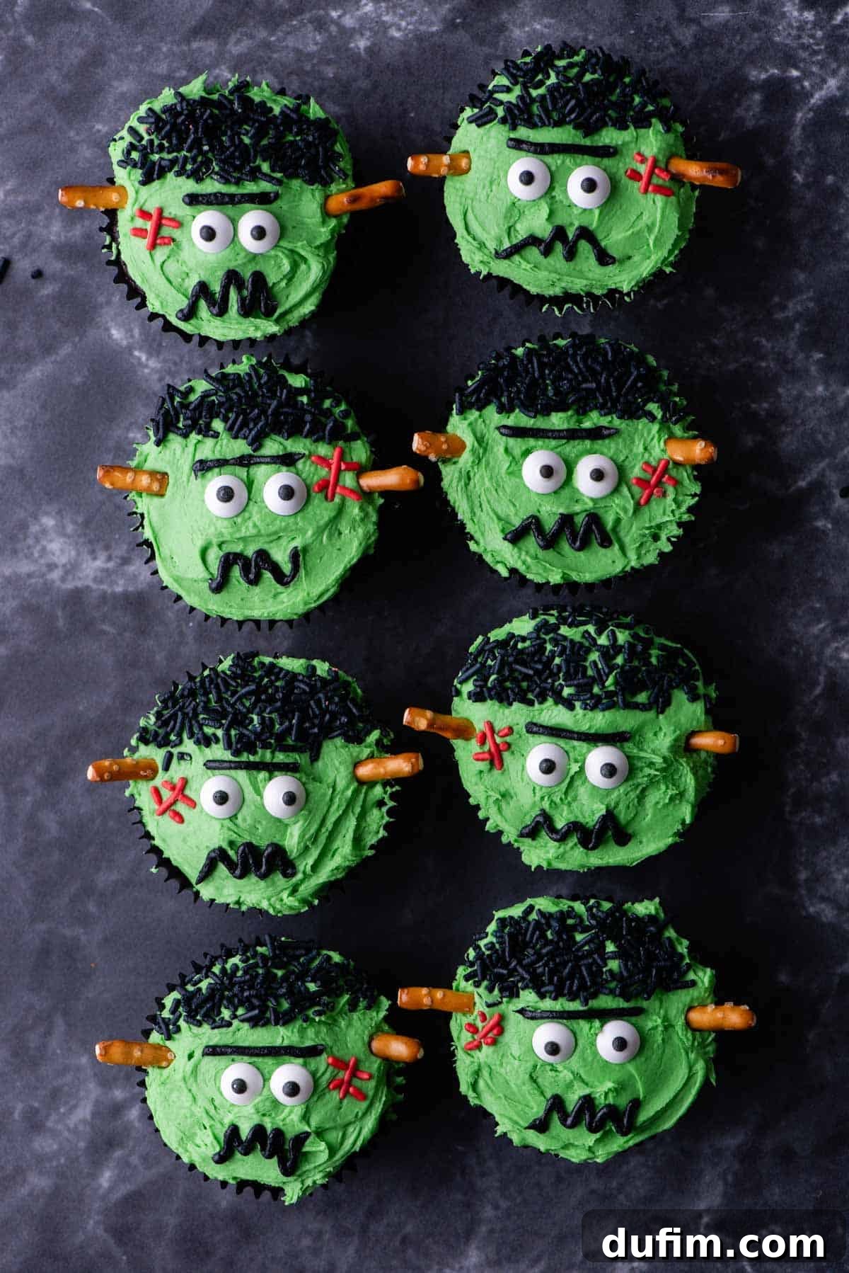 Rows of freshly baked chocolate Frankenstein cupcakes neatly arranged on a grey surface, waiting to be decorated.